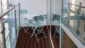 Uma varanda com piso de madeira, guarda-corpo de metal e duas cadeiras dobráveis verdes.