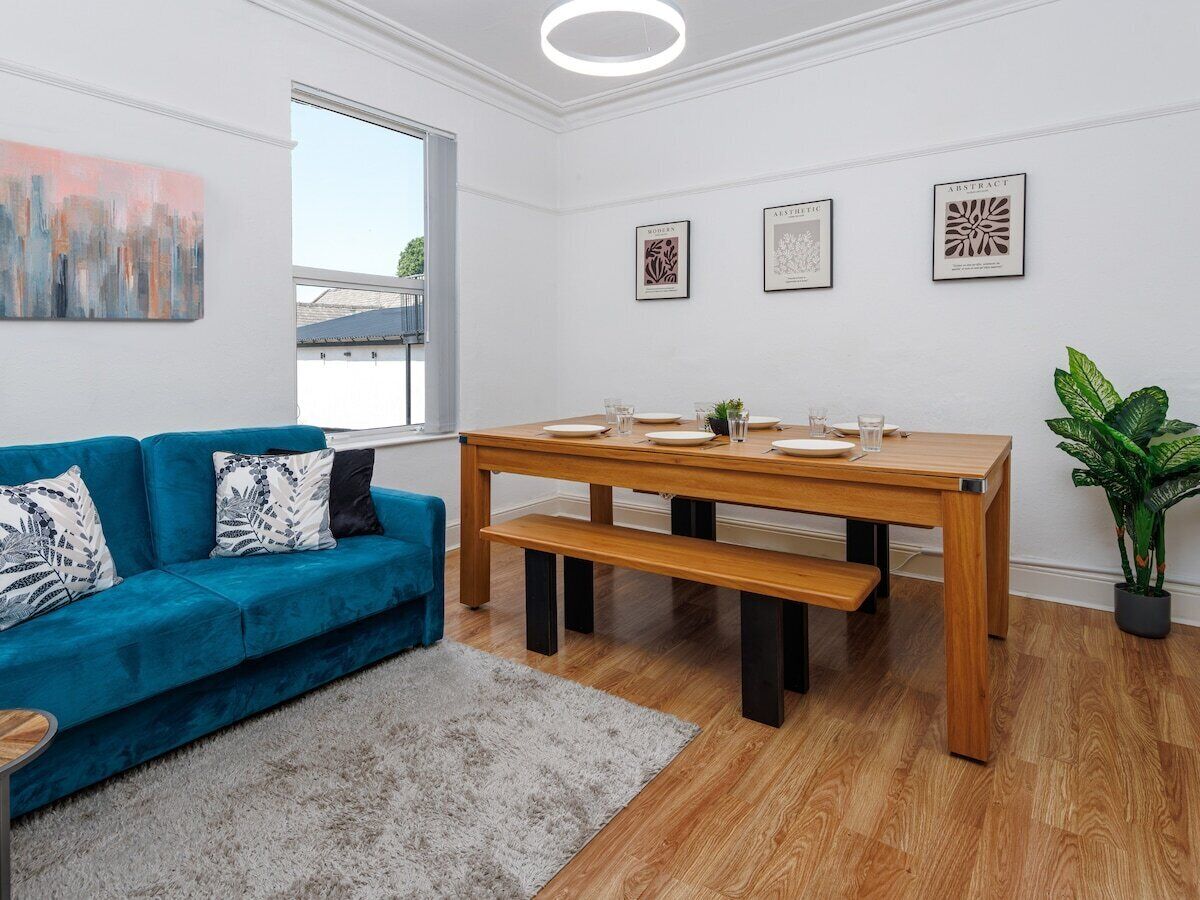 Una sala de estar moderna con un sofá azul, una mesa de comedor de madera y una planta en maceta.