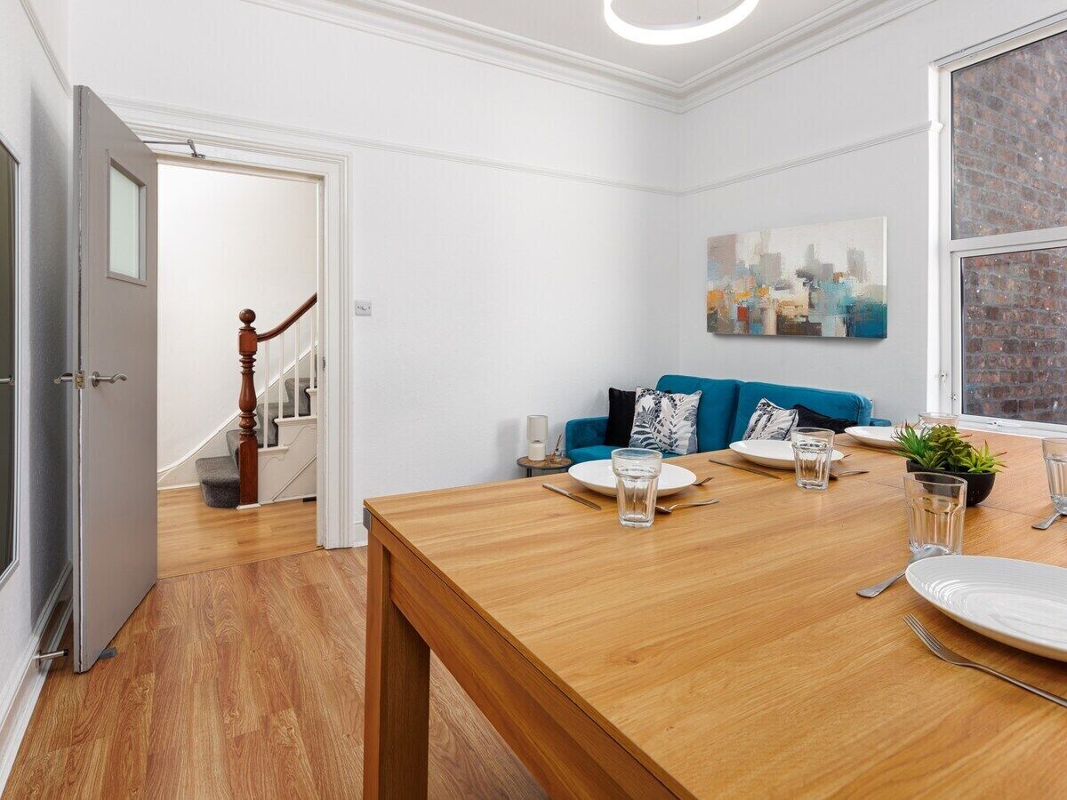 Een eetgedeelte met een houten tafel gedekt voor twee personen, een blauwe bank en een trap op de achtergrond.