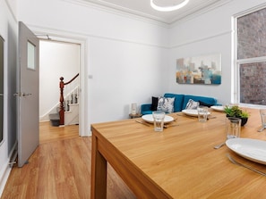 Ein Essbereich mit einem Holztisch, gedeckt für zwei Personen, einem blauen Sofa und einer Treppe im Hintergrund.