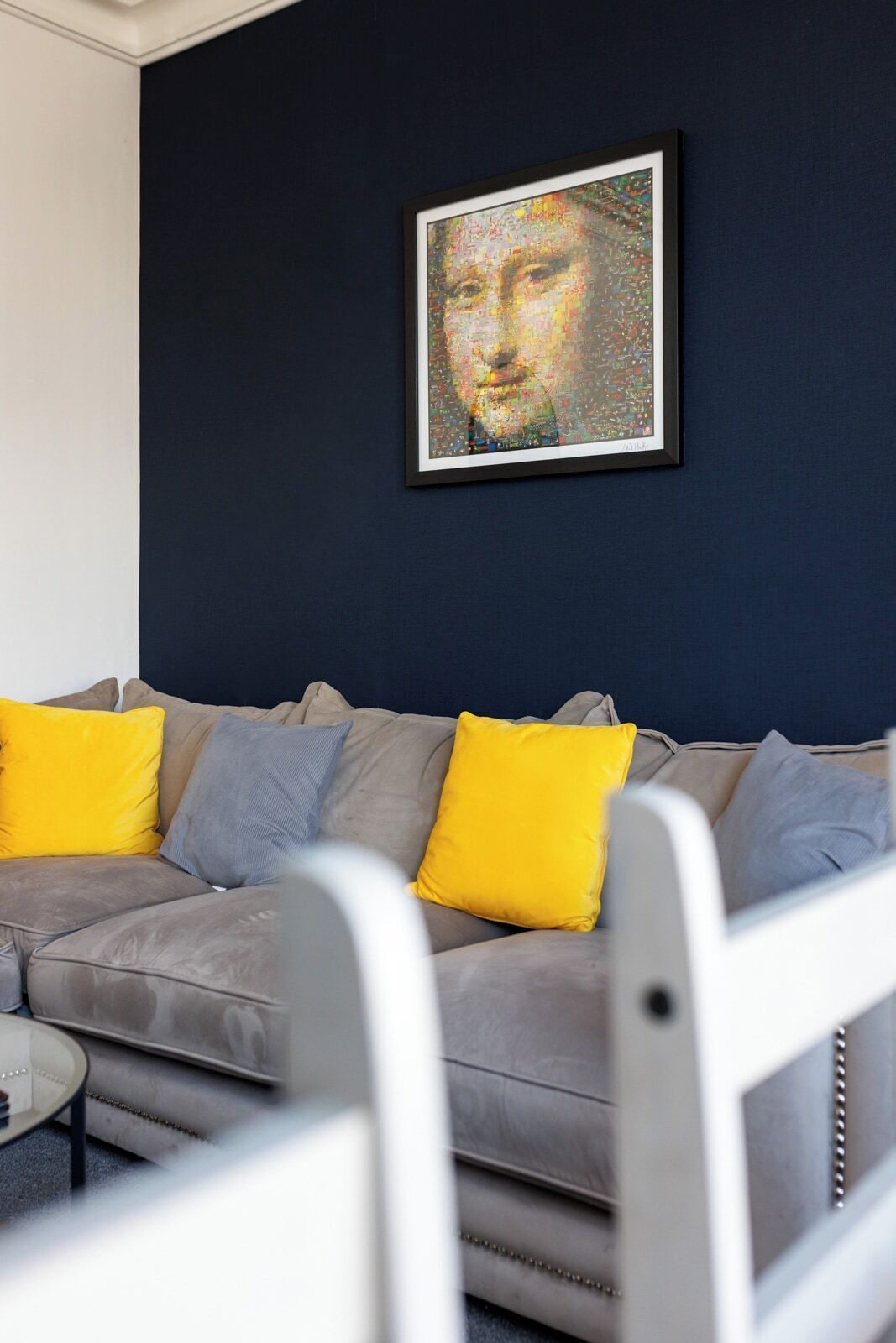 A living room with a grey sofa, yellow and grey cushions, and a framed artwork on the wall.