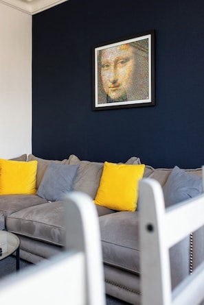 Ein Wohnzimmer mit einem grauen Sofa, gelb-grauen Kissen und einem gerahmten Kunstwerk an der Wand.
