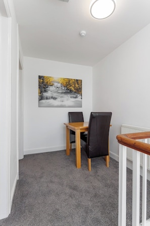 A dining area with a table and chairs, a painting on the wall, and a ceiling light. - Flatzy- Sleeps 16 Near Football Ground + Ping Pong (Liverpool)