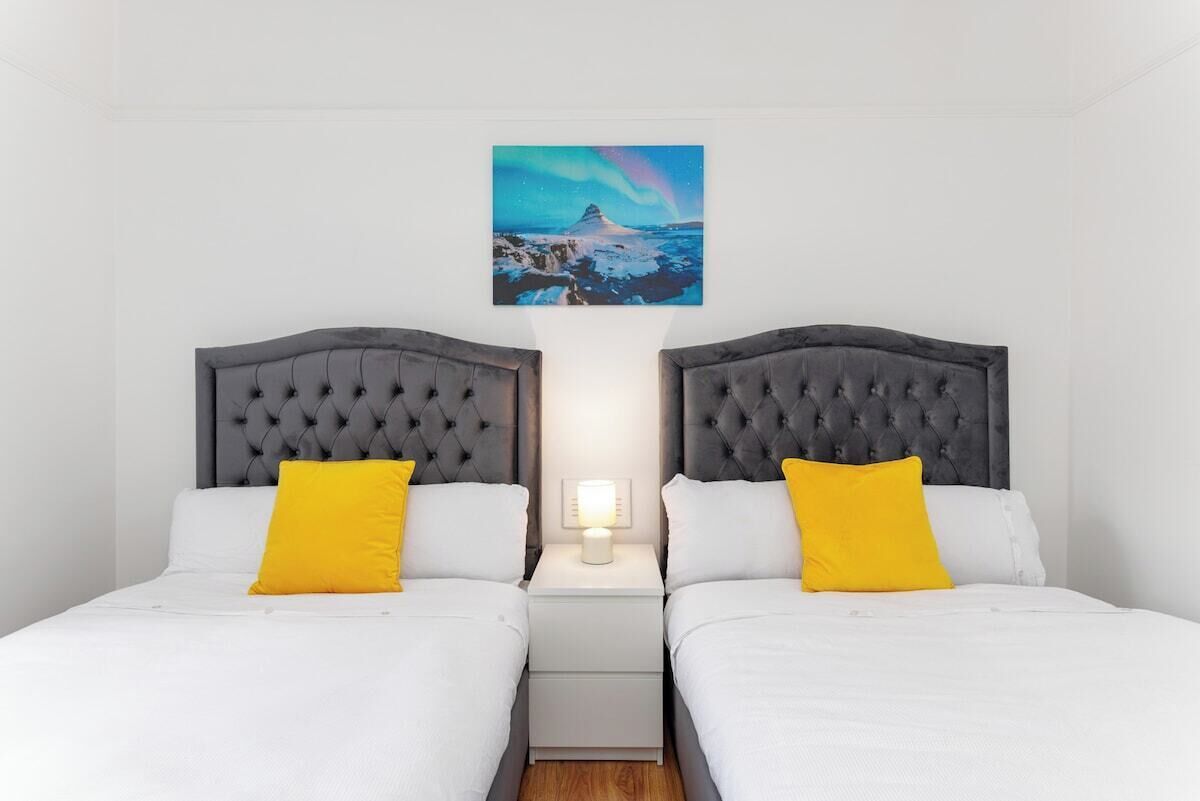 A double bed room with two nightstands, each with a lamp, and a painting of a mountain landscape above the bed.