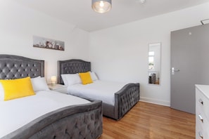 A hotel room with two beds, a grey door, and a small white cabinet. - Flatzy- Sleeps 16 Near Football Ground + Ping Pong (Liverpool)