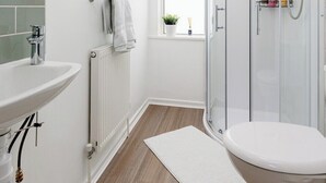 Ein modernes Badezimmer mit einer Duschkabine aus Glas, einem weißen Waschbecken und einem Fenster mit Aussicht.