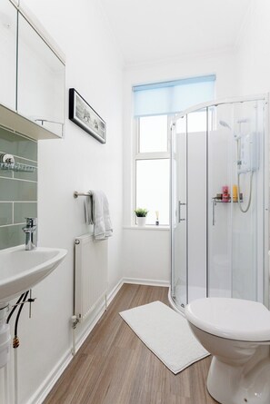 Ein modernes Badezimmer mit einer Duschkabine aus Glas, einem weißen Waschbecken und einem Fenster mit Aussicht.