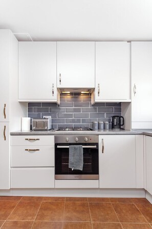 A modern kitchen with white cabinets, a gas stove, a microwave, and a coffee maker. - Flatzy- Sleeps 16 Near Football Ground + Ping Pong (Liverpool)