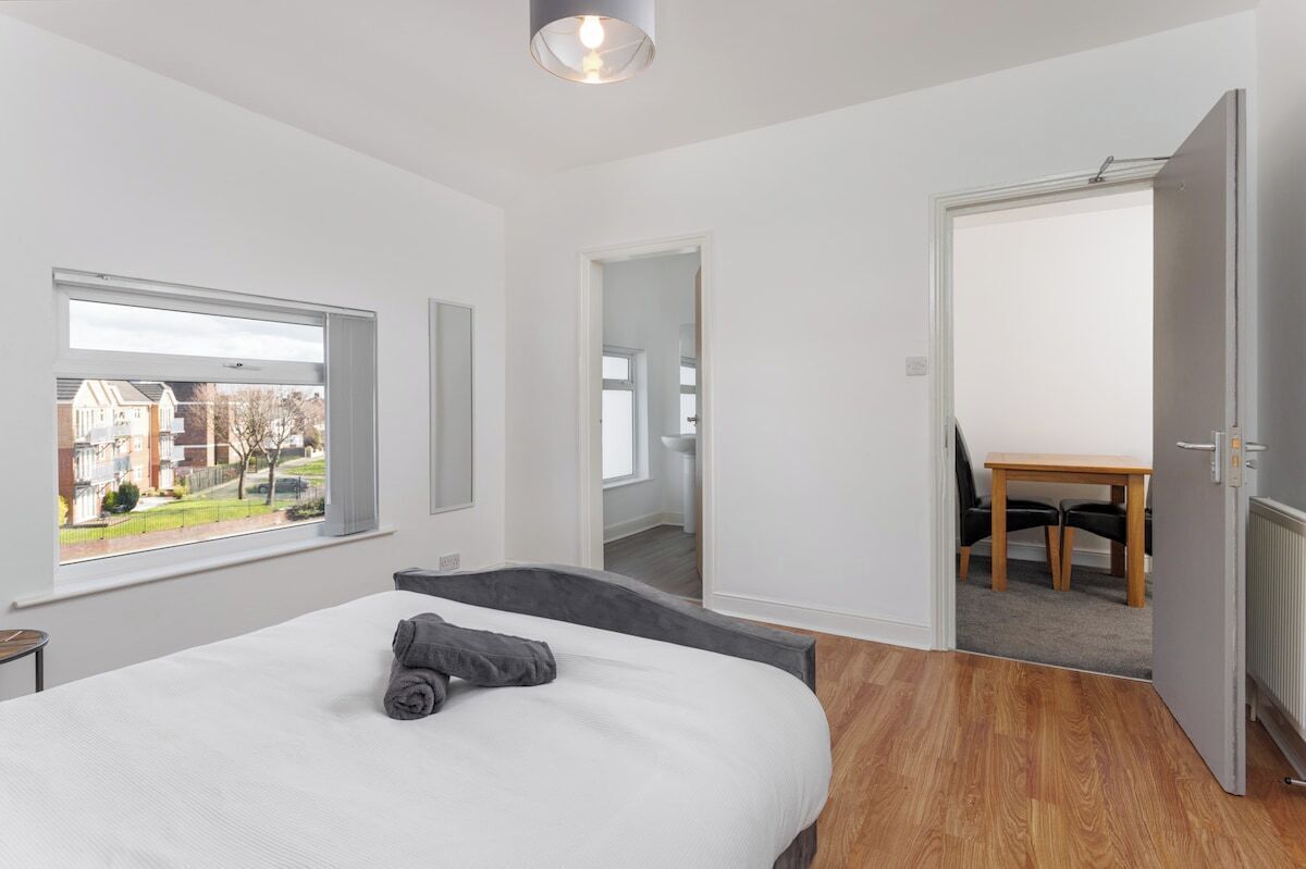Un dormitorio moderno con una cama grande, una ventana con vistas, una puerta que da al baño y una pequeña mesa con sillas.