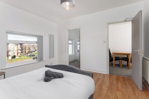 Ein modernes Schlafzimmer mit einem großen Bett, einem Fenster mit Blick, einer Tür zu einem Badezimmer und einem kleinen Tisch mit Stühlen.