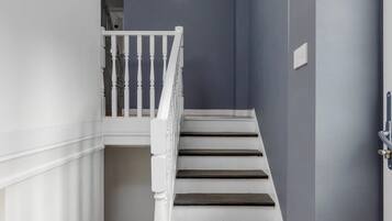 Una escalera con balaustres blancos y peldaños oscuros, que conduce a un rellano con un cuadro enmarcado.