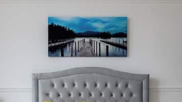 Un dormitorio con cabecera capitonada, cama con ropa blanca y dos almohadas amarillas, y un cuadro de un muelle en la pared.