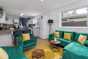 Un soggiorno moderno con divani verdi, un tavolino in legno e una cucina sullo sfondo.