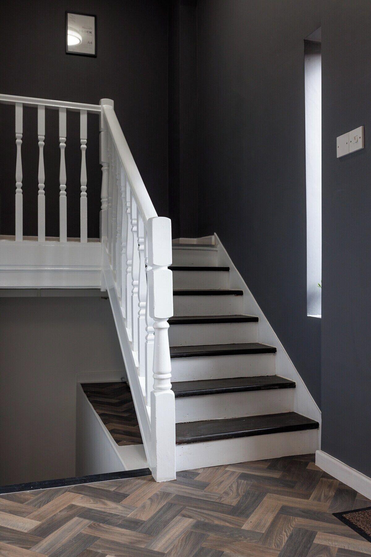A staircase with white balusters and dark steps, leading to a landing with a small window.