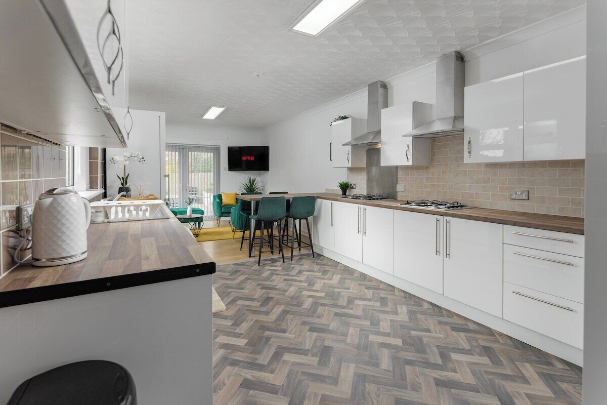 Een moderne keuken met witte kasten, een visgraat parketvloer en een flatscreen televisie aan de muur.