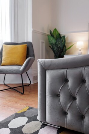 A tufted grey sofa with a cushion, a grey armchair with a yellow pillow, and a patterned rug.