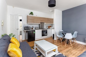 A modern kitchen with a dining area, a sofa with cushions, and a small table. - Flatzy - Sefton Park Abode (10 min to City Centre) (Liverpool)
