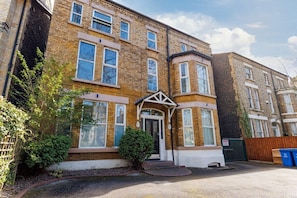 A two-story brick house with a front entrance, a small porch, and a garden area with a tree and shrubs. - Flatzy - Sefton Park Abode (10 min to City Centre) (Liverpool)