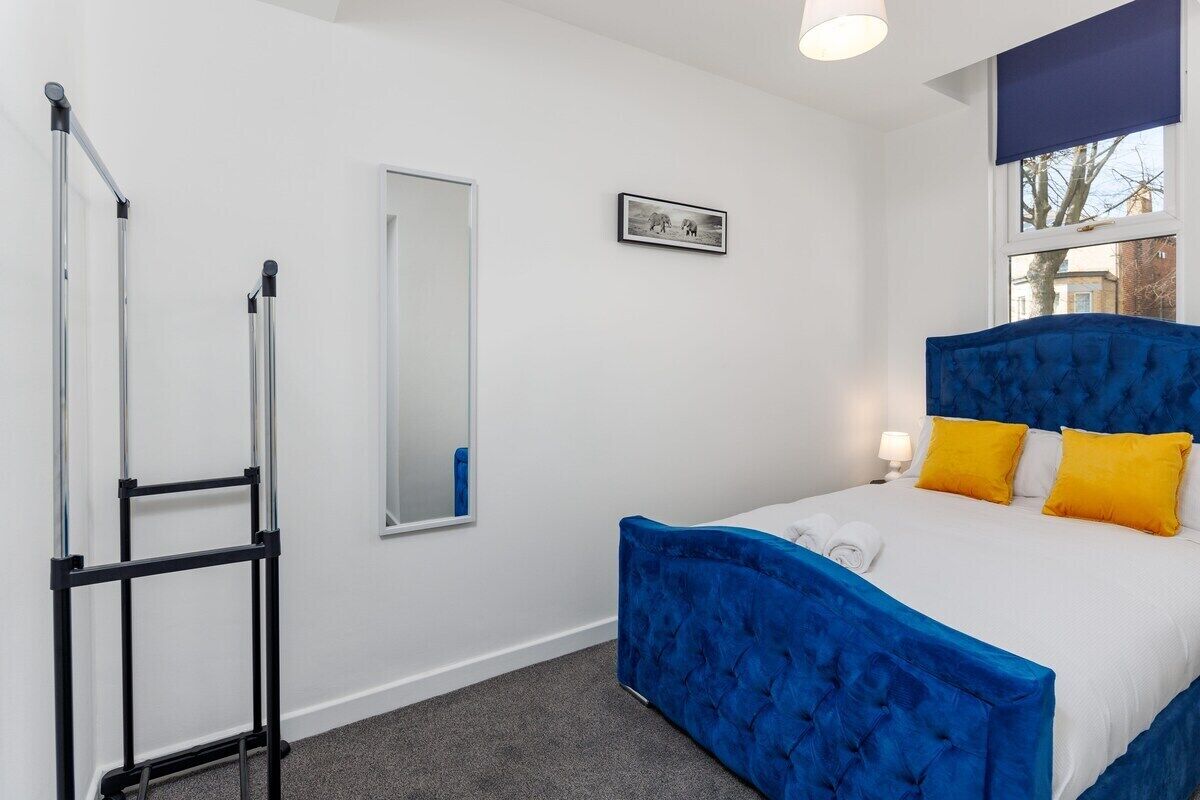 A bedroom with a bed, a mirror, a picture on the wall, and a window with a view.