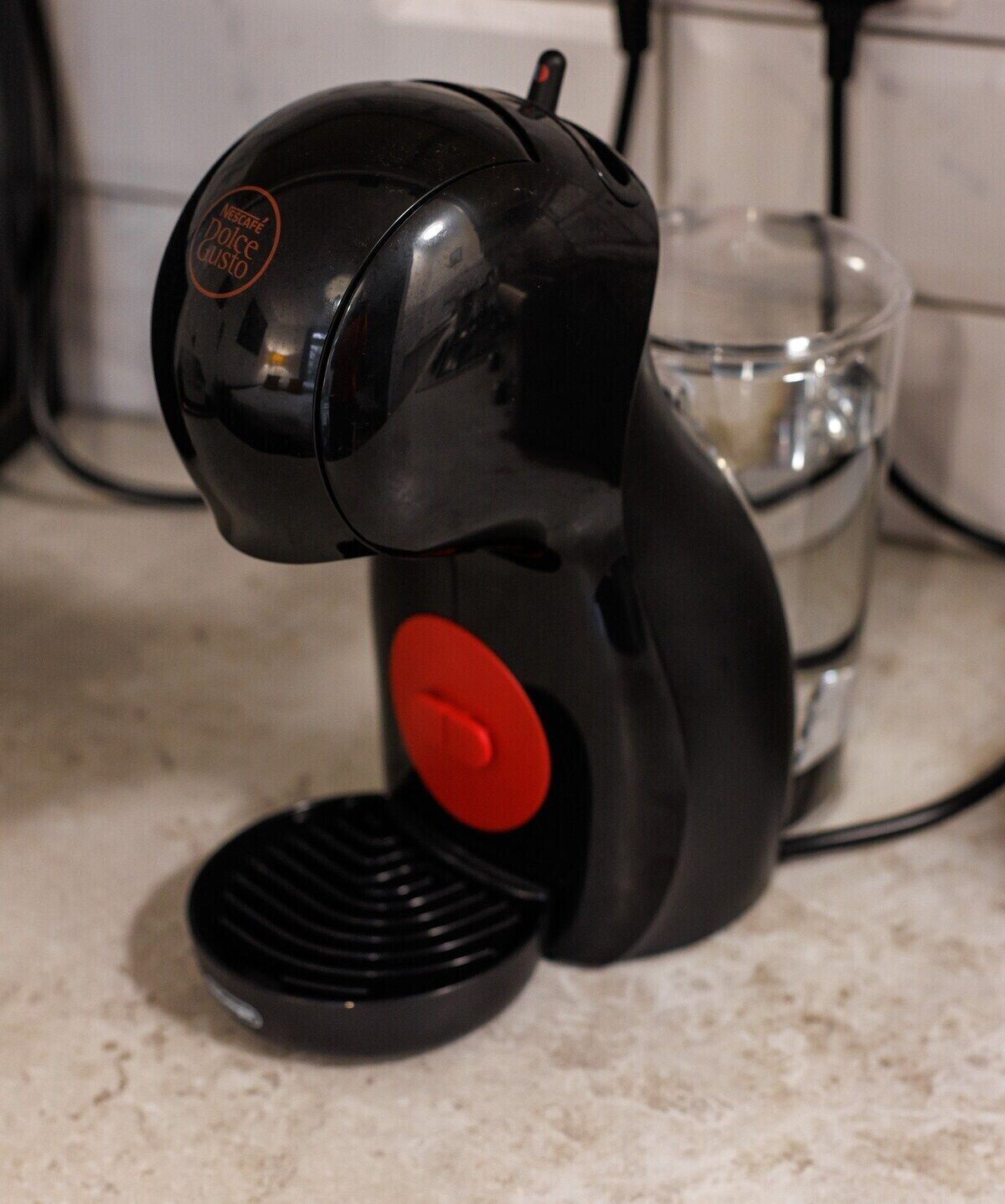 A black coffee machine with a red button, placed on a kitchen counter.