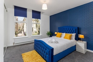 A bedroom with a large bed, two bedside tables, a window with blinds, and a patterned wall. - Flatzy - Sefton Park Abode (10 min to City Centre) (Liverpool)