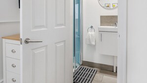 A modern bathroom with a white door, a blue shower, a round mirror, and a white sink.