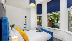 Ein Schlafzimmer mit Bett, Lampe, Fenster mit Jalousien und Blick ins Grüne.