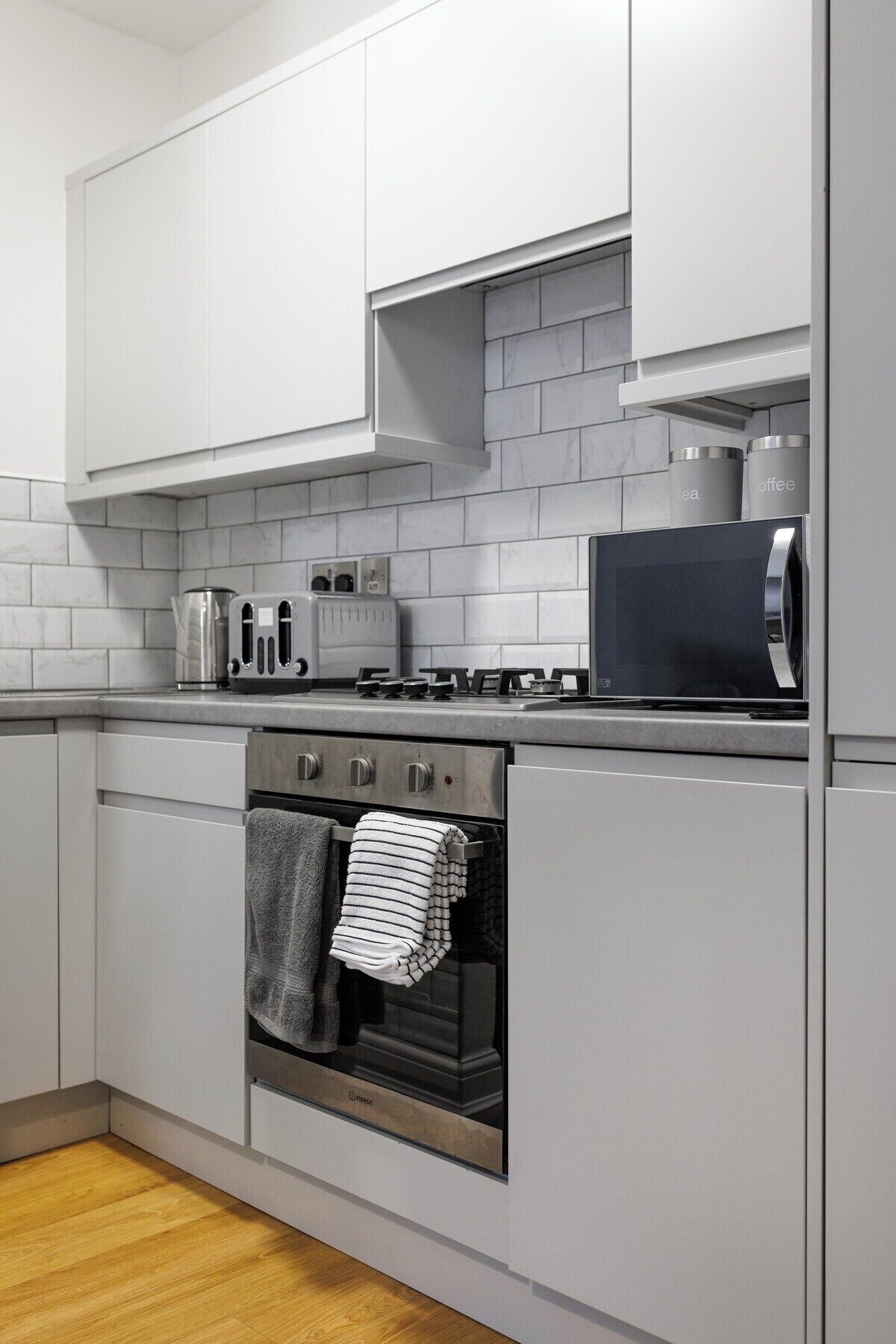 A modern kitchen with white cabinets, a stainless steel range, a microwave, and a toaster.