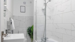 Ein modernes Badezimmer mit einer gläsernen Duschkabine, einem weißen Waschbecken und einer Topfpflanze.