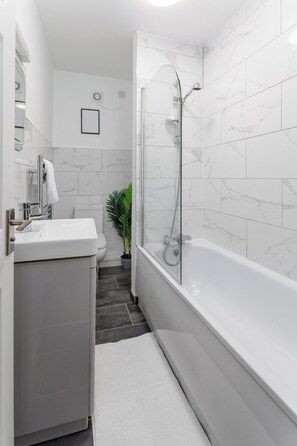 Un bagno moderno con cabina doccia in vetro, lavabo bianco e una pianta in vaso.