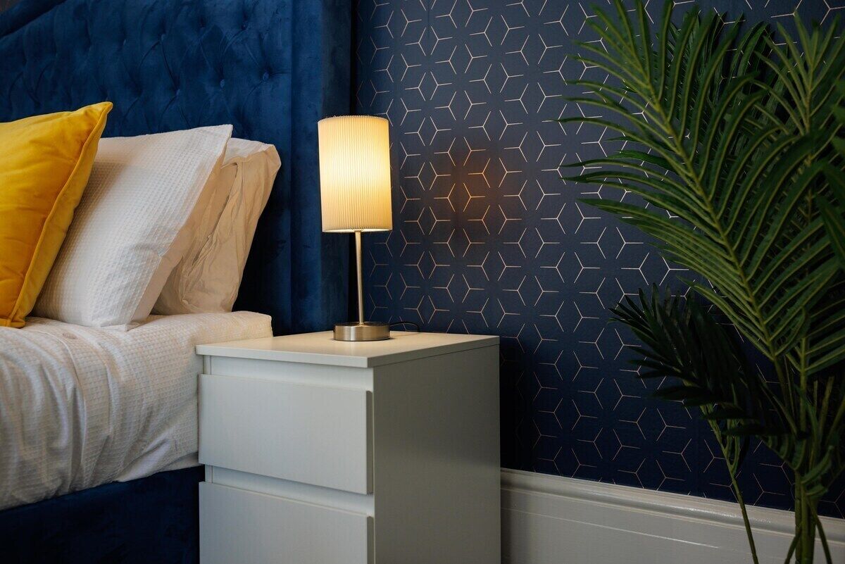 Un letto con una testiera blu, una lampada da comodino e una pianta in vaso.