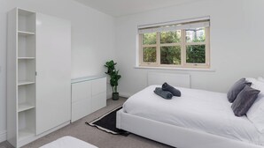 Un dormitorio con cama, armario blanco, planta en maceta y ventana con vistas a la vegetación.