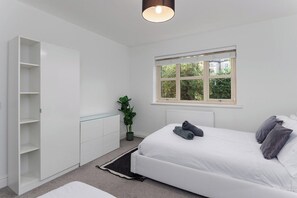 A bedroom with a bed, a white wardrobe, a potted plant, and a window with a view of greenery. - Flatzy - Quiet Sefton Park Luxury Apartment (Liverpool)