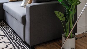 Una sala de estar moderna con un sofá gris, una planta en maceta y una lámpara de pared.