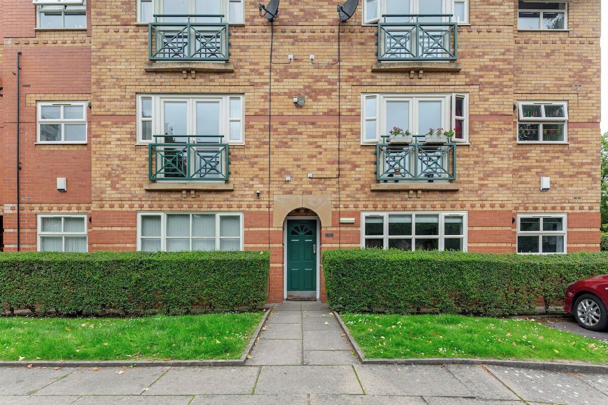 A multi-story residential building with balconies, a central entrance, and a red car parked on the street.