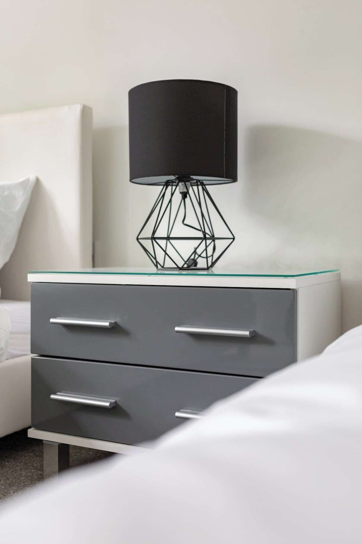 A modern bedside table with a glass top and a black lamp with a geometric base.