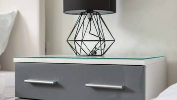 A modern bedside table with a glass top and a black lamp with a geometric base.
