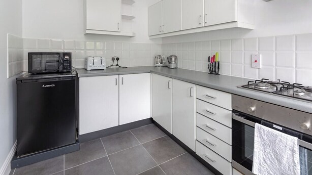 Una cocina moderna con armarios blancos, un microondas, un tostador, una cafetera y una estufa a gas.