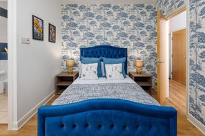 A bedroom with a large bed, two bedside tables with lamps, and a door leading to another room. - Flatzy - Spacious City Centre Retreat  Sleeps 6 (Merseyside)