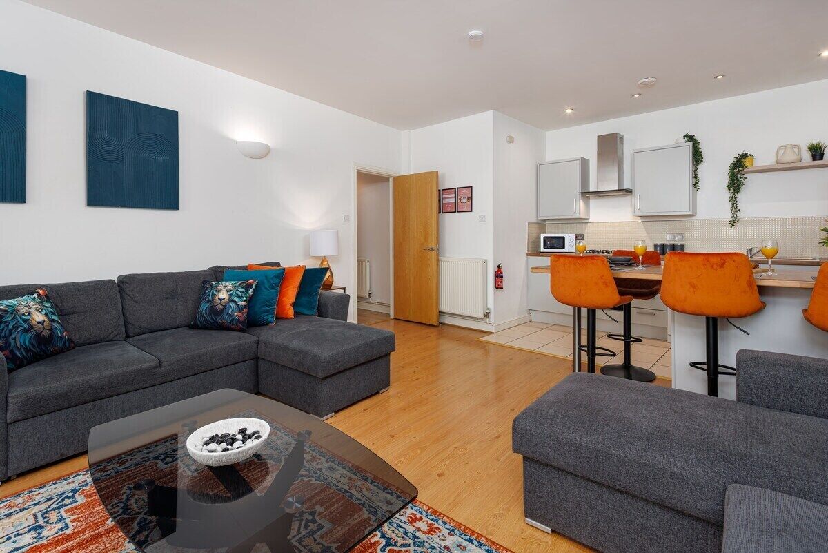 A modern living room with a grey sofa set, a coffee table, and a kitchen area with bar stools.