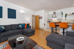 Ein modernes Wohnzimmer mit einer grauen Sofagarnitur, einem Couchtisch und einer Küchenzeile mit Barhocker.