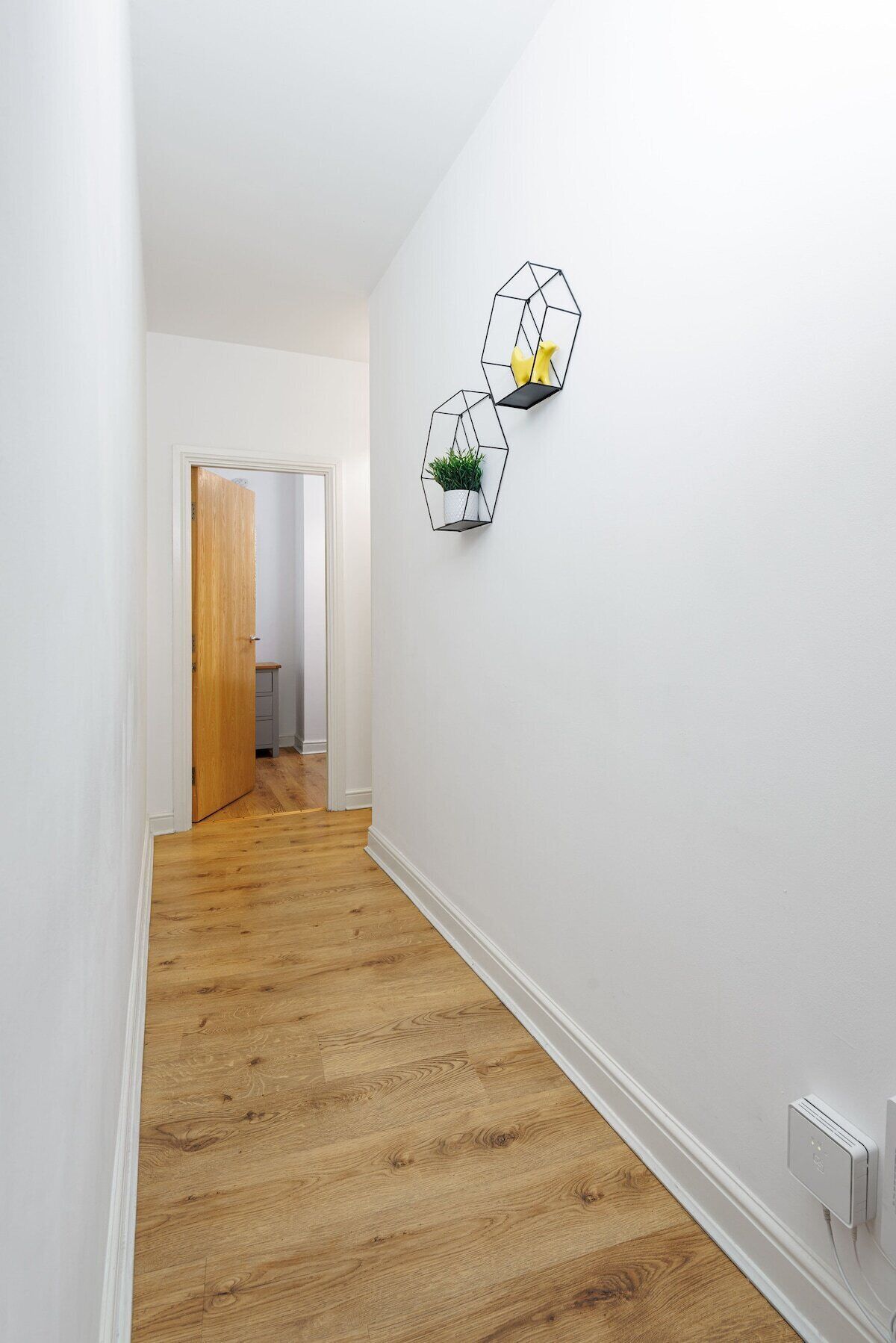 A hallway with wooden flooring, white walls, and geometric wall art.