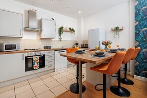 Una cucina moderna con mobili bianchi, un forno a microonde, un piano cottura a gas e un'area pranzo con un tavolo di legno e sedie arancioni.