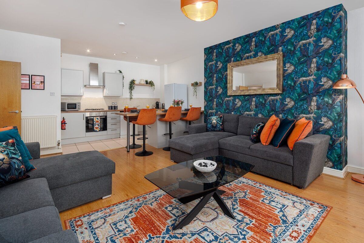 A modern living room with a grey sectional sofa, a glass coffee table, and a patterned rug.
