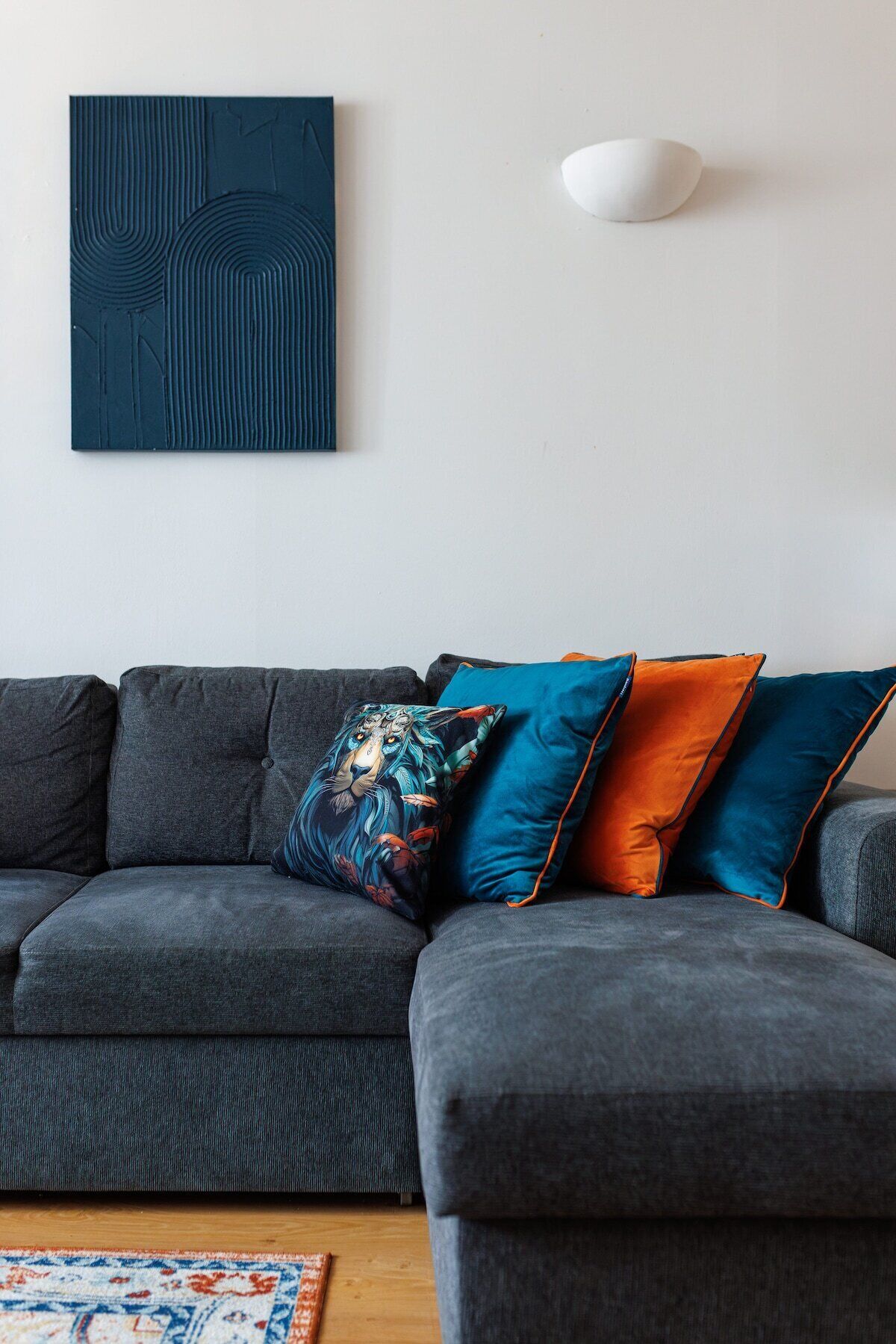 Un canapé d’angle gris avec plusieurs coussins, un tapis à motifs et un luminaire fixé au mur.