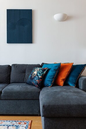 Ein graues Ecksofa mit vielen Kissen, einem gemusterten Teppich und einer Wandleuchte.