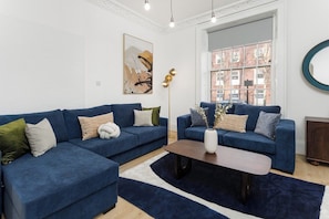 Un soggiorno moderno con due divani blu, un tavolino da caffè e un'ampia finestra vista edifici.
