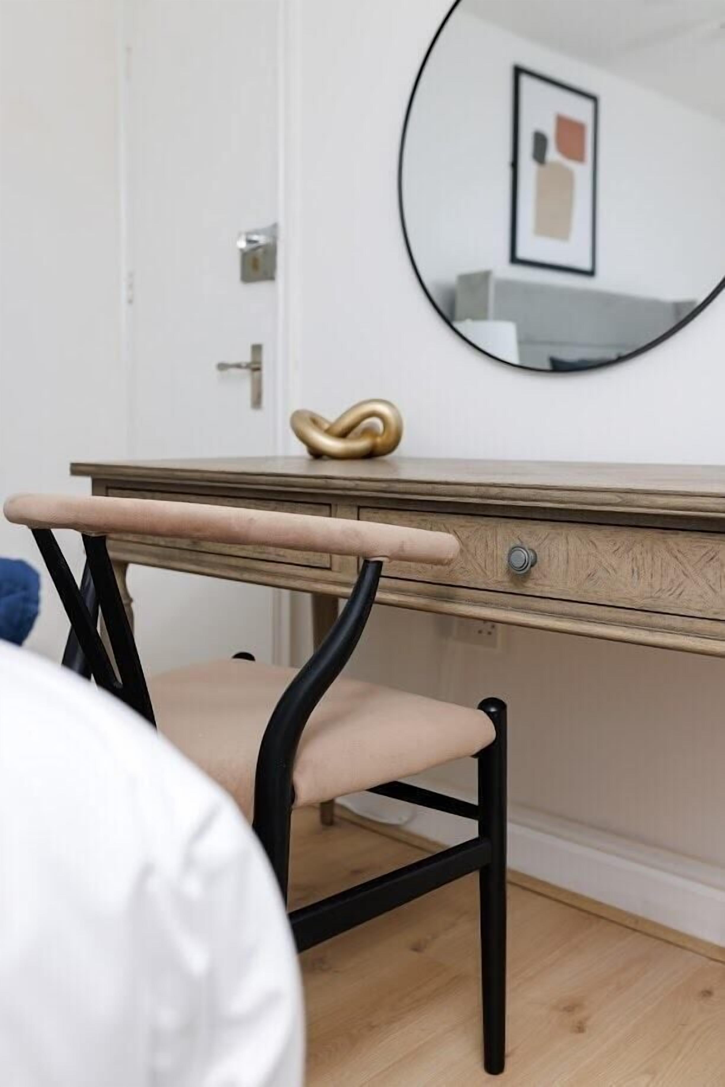 A room with a wooden desk, a chair, a mirror, and a framed picture on the wall.