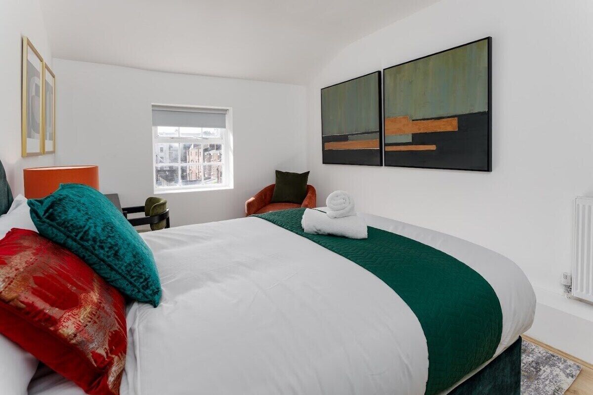 Quarto de hotel com cama, janela, uma cadeira e obras de arte na parede.