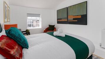 Quarto de hotel com cama, janela, uma cadeira e obras de arte na parede.